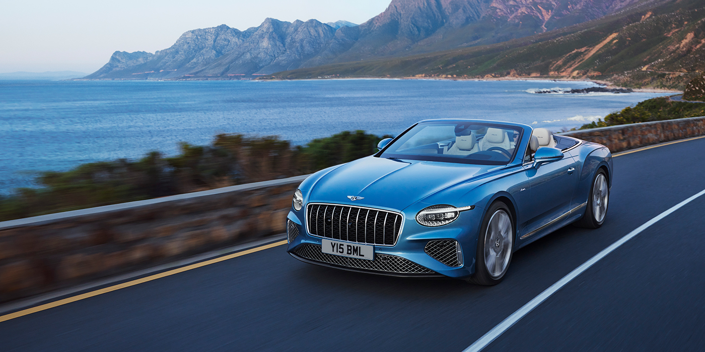 Bentley Hannover New Bentley Continental GTC Azure convertible in Light Windsor blue paint with 22 inch Azure wheels and chrome grill, driving dynamically by the sea