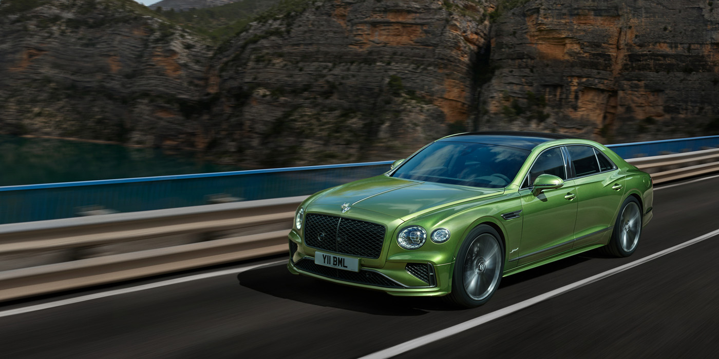 Bentley Hannover Bentley New Flying Spur Speed v8 hybrid sedan driving dynamically on a mountain road in Tourmaline Green paint