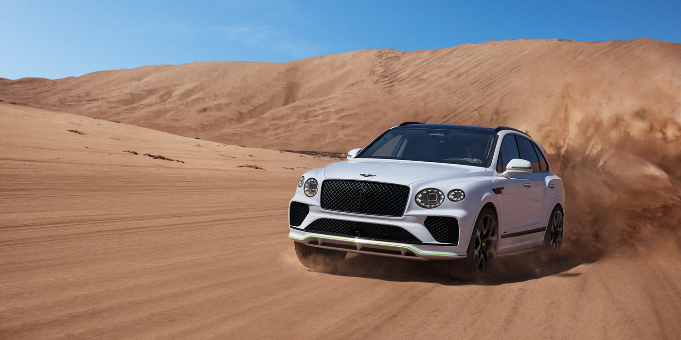 Bentley Hannover Bentley Bentayga Speed SUV front three quarter in Snow Quarts Pearlescent by Mulliner white paint driving dynamically through the desert