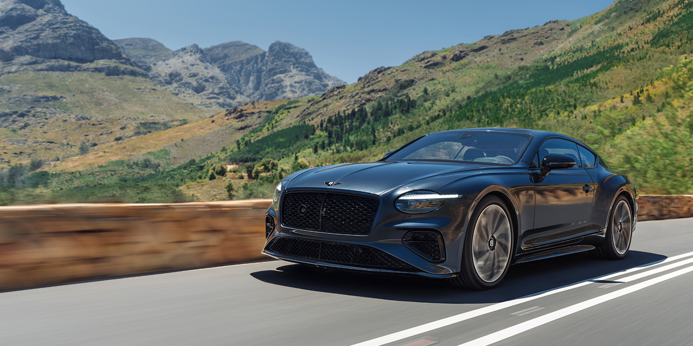 Bentley Hannover Bentley Continental GT coupe in Thunder paint and 22" ten swept spoke wheels front 3/4 driving on mountain road