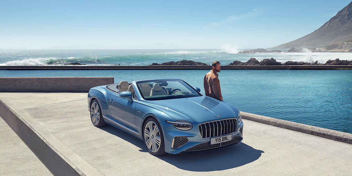 Bentley Hannover New Bentley Continental GTC Azure convertible front view in Light Windsor blue paint with 22 inch ten spoke wheels parked by the sea in the sunshine
