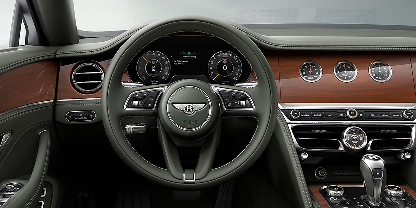Bentley Hannover New Bentley Flying Spur sedan front cabin in Cumbrian Green hide and Crown Cut walnut veneer showing steering wheel and Rotating Display with three clocks on face