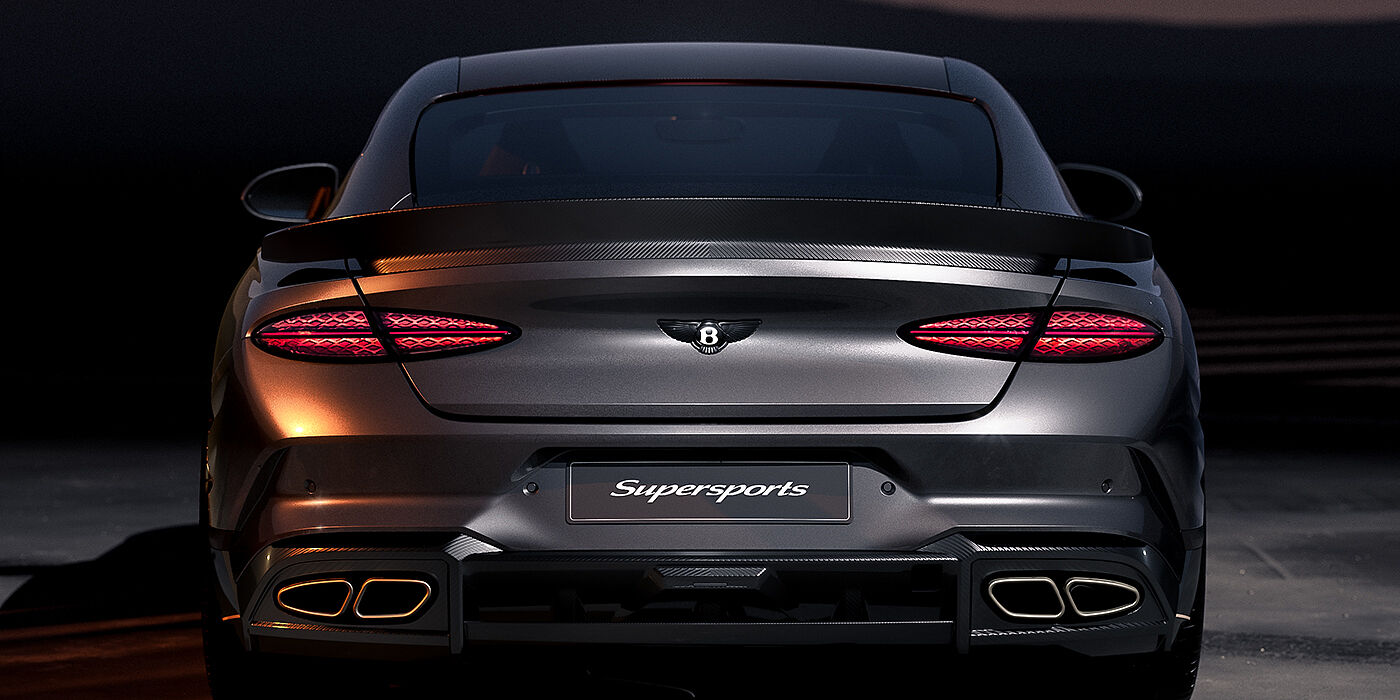 Bentley Hannover Bentley Supersports rear view with illuminated rear lamps, spoiler and black Bentley badge in Anthracite paint against a dark grey and red background