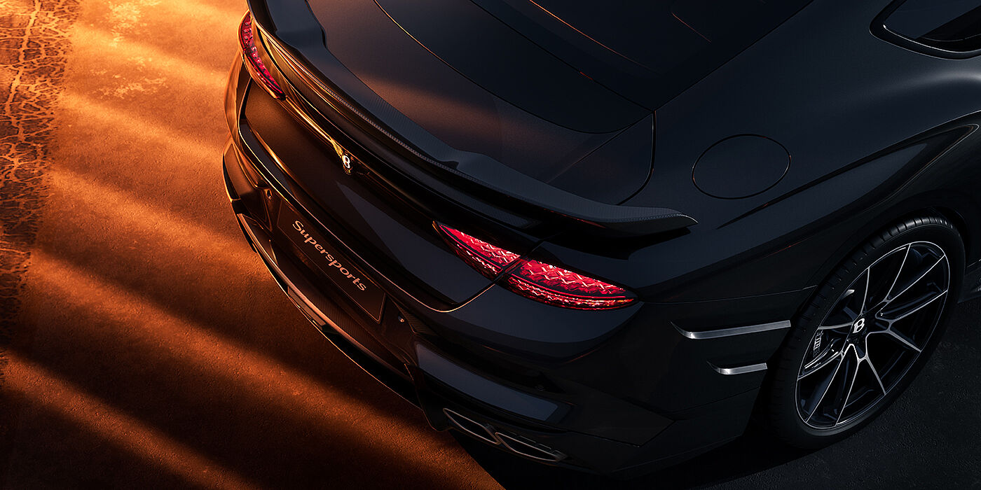 Bentley Hannover Bentley Supersports rear overhead view showing illuminated rear lamps and Supersports Forged Alloy wheel in Anthracite paint against a dark grey and red background