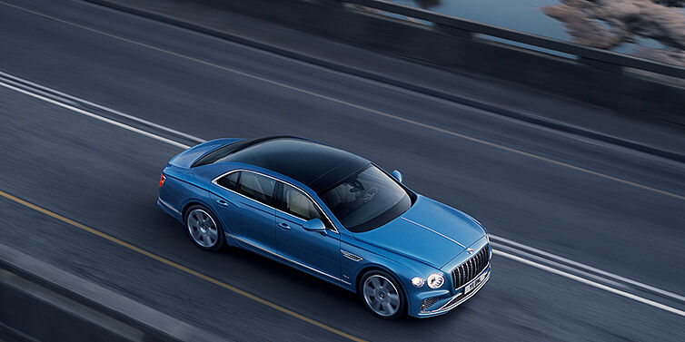 Bentley Hannover New Bentley Flying Spur Azure sedan in Light windsor blue paint by Mulliner, with 22 inch Azure wheels seen from overhead driving dynamically on a country road