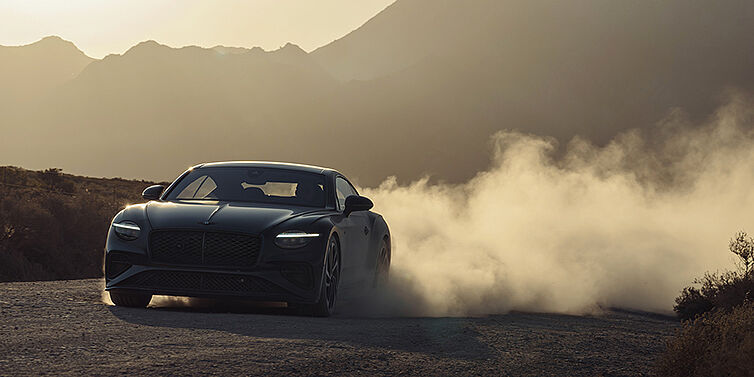 Bentley Hannover Bentley Continental GT Coupé in Thunder Lackierung vorne 3/4 bei Sonnenuntergang mit Staubwolke
