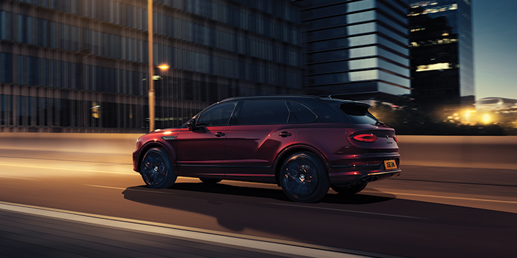 Bentley Hannover Bentley Bentayga Extended Wheelbase Mulliner SUV in Cricket Ball red paint driving dynamically in city at night